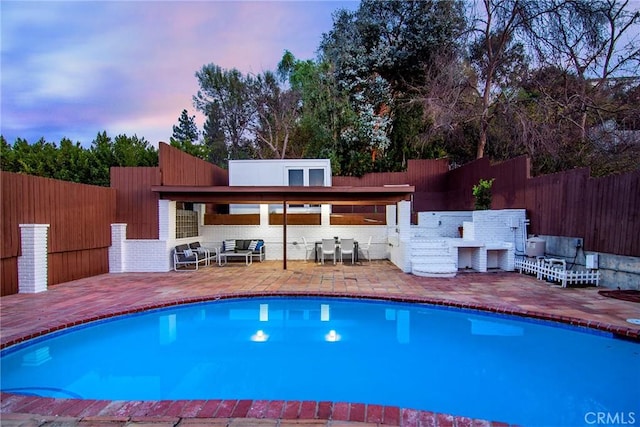 pool at dusk with a patio and an outdoor bar