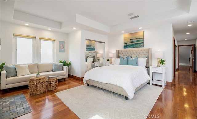 bedroom with a tray ceiling, wood finished floors, visible vents, and recessed lighting