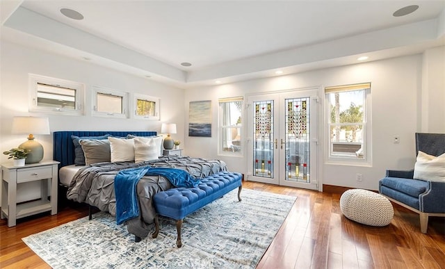 bedroom with access to exterior, wood-type flooring, a raised ceiling, and french doors