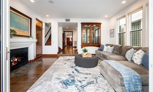 living room featuring a glass covered fireplace, visible vents, baseboards, and recessed lighting