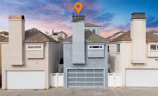 view of front of house featuring a garage, a tiled roof, a chimney, and stucco siding