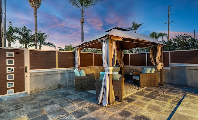 patio terrace at dusk featuring a gazebo, fence, and an outdoor living space