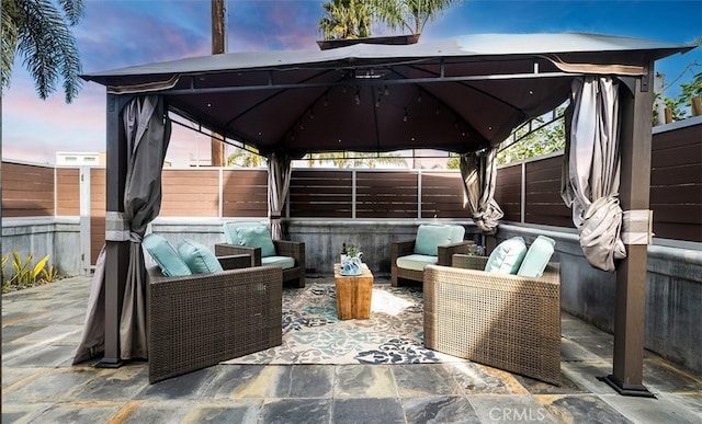 patio terrace at dusk featuring a fenced backyard, an outdoor living space, and a gazebo