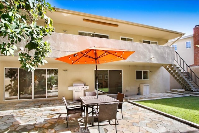 rear view of house with a patio area, stairway, outdoor dining area, and stucco siding