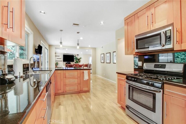 kitchen with sink, dark stone counters, hanging light fixtures, light hardwood / wood-style floors, and stainless steel appliances