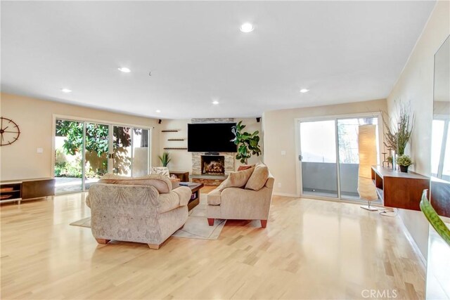 living room featuring a stone fireplace, a wealth of natural light, and light hardwood / wood-style flooring