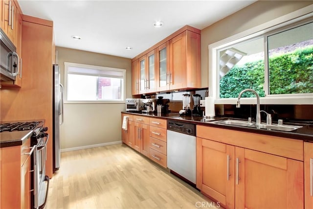 kitchen featuring stainless steel appliances, dark countertops, glass insert cabinets, light wood-style floors, and a sink