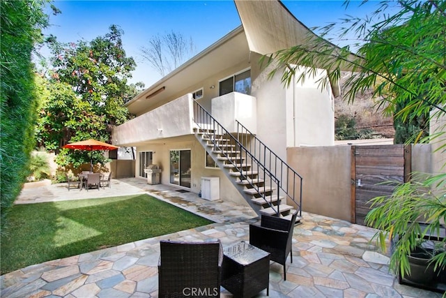 back of property featuring a patio, fence, a yard, stairway, and stucco siding