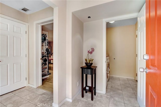 hallway featuring light tile patterned flooring, washing machine and dryer, visible vents, and baseboards