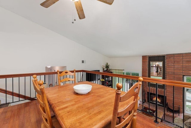 dining area featuring a brick fireplace, hardwood / wood-style flooring, and vaulted ceiling