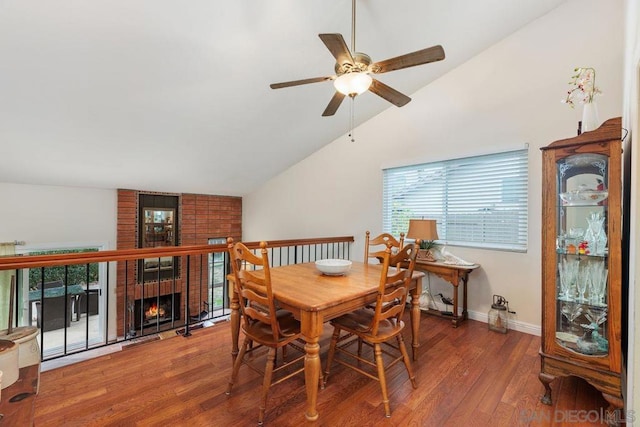 dining room with a brick fireplace, hardwood / wood-style flooring, vaulted ceiling, and ceiling fan