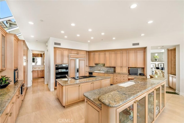 kitchen featuring sink, light brown cabinets, paneled fridge, an island with sink, and light stone countertops