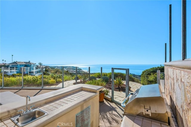 balcony featuring a water view, grilling area, an outdoor kitchen, and sink