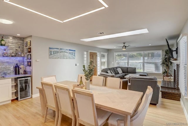 dining room with indoor bar, wine cooler, ceiling fan, and light hardwood / wood-style flooring