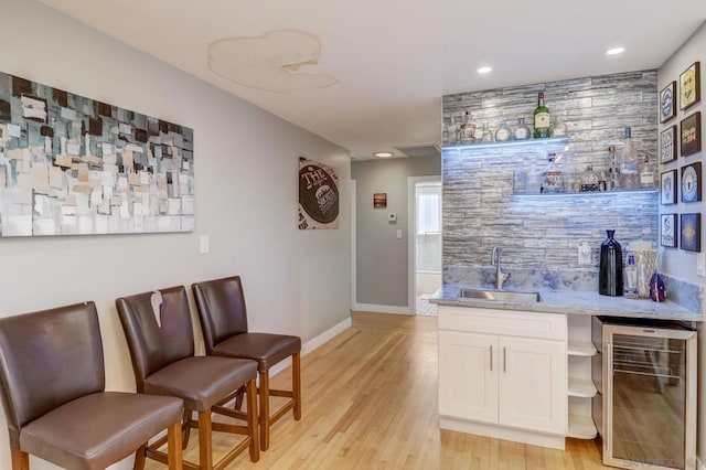 bar featuring wine cooler, sink, white cabinetry, light hardwood / wood-style floors, and decorative backsplash