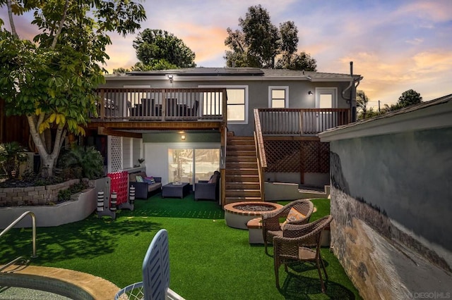 back house at dusk featuring a wooden deck, an outdoor living space, and a lawn