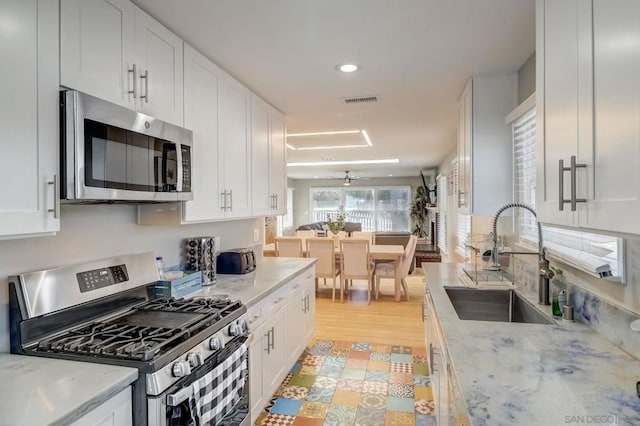 kitchen featuring appliances with stainless steel finishes, white cabinetry, sink, light hardwood / wood-style floors, and light stone countertops