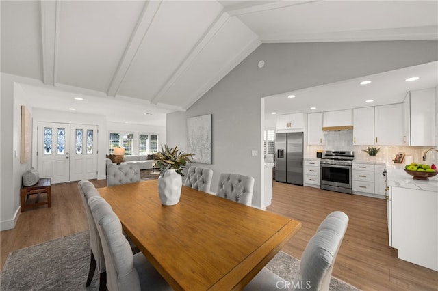 dining area with sink, beam ceiling, light hardwood / wood-style flooring, and high vaulted ceiling