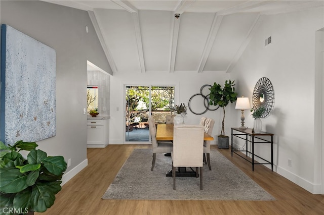 dining area with beamed ceiling, high vaulted ceiling, and light hardwood / wood-style flooring