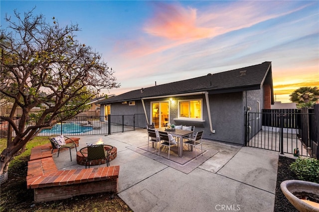 back house at dusk with a fenced in pool, a patio area, and an outdoor fire pit