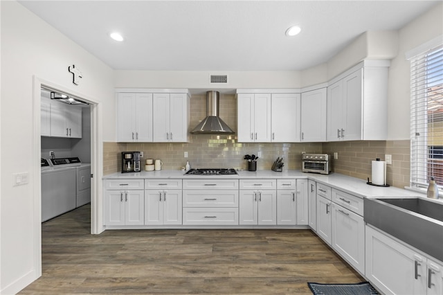 kitchen with white cabinetry, wall chimney range hood, and washer and dryer