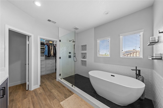 bathroom with plus walk in shower, hardwood / wood-style floors, and tile walls