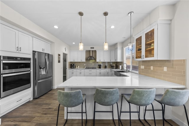 kitchen featuring pendant lighting, white cabinets, wall chimney exhaust hood, and appliances with stainless steel finishes