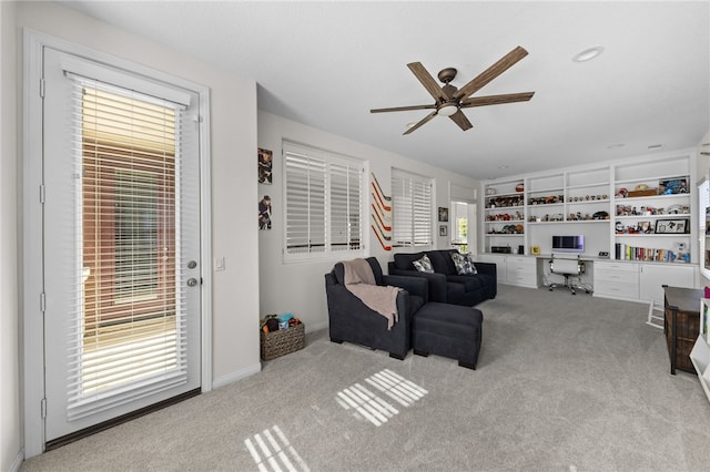 carpeted living room with built in desk and ceiling fan