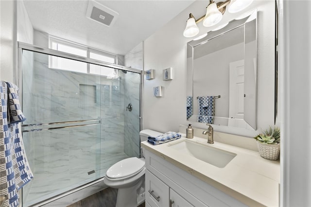 bathroom featuring vanity, toilet, a shower with shower door, and a textured ceiling