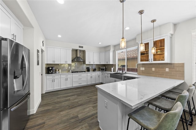 kitchen featuring hanging light fixtures, stainless steel refrigerator with ice dispenser, wall chimney range hood, and kitchen peninsula