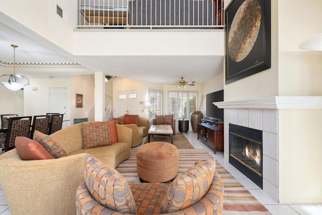 living room featuring ceiling fan, a towering ceiling, a tile fireplace, and light tile patterned floors