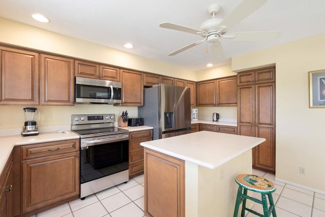 kitchen with light tile patterned floors, ceiling fan, appliances with stainless steel finishes, a kitchen breakfast bar, and a center island