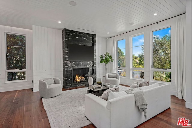 living room with a high end fireplace, wooden walls, wooden ceiling, and dark hardwood / wood-style flooring