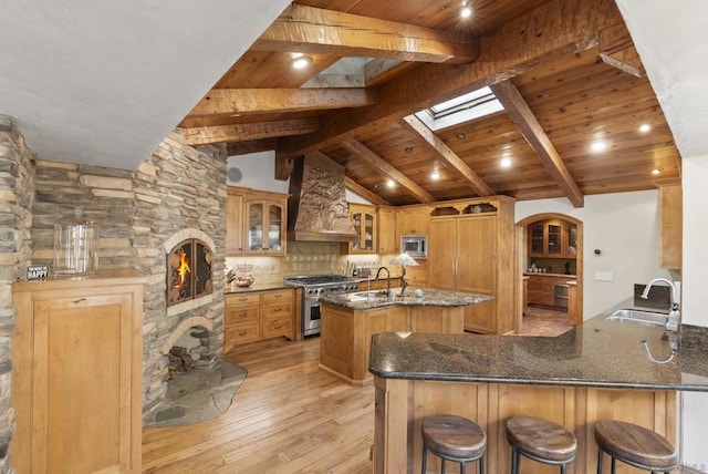 kitchen featuring lofted ceiling with skylight, sink, custom exhaust hood, appliances with stainless steel finishes, and kitchen peninsula