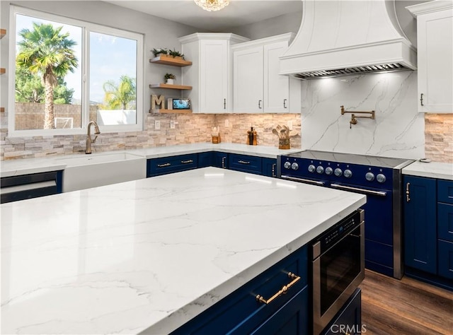 kitchen featuring blue cabinetry, sink, custom exhaust hood, range, and stainless steel microwave