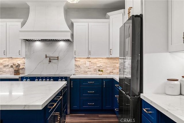 kitchen featuring white cabinetry, black fridge, custom range hood, and blue cabinetry