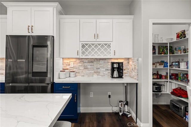 kitchen with blue cabinets, white cabinetry, light stone counters, stainless steel fridge, and dark hardwood / wood-style flooring