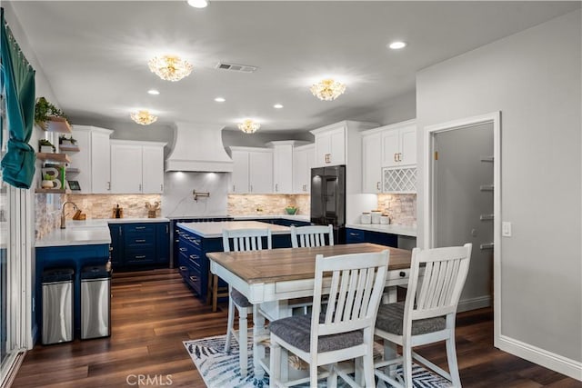 kitchen with white cabinetry, blue cabinets, black fridge, and custom exhaust hood