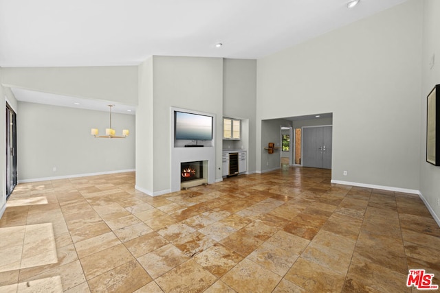 unfurnished living room with a notable chandelier, wine cooler, and high vaulted ceiling