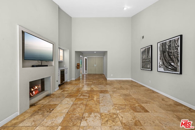 unfurnished living room featuring a towering ceiling and wine cooler