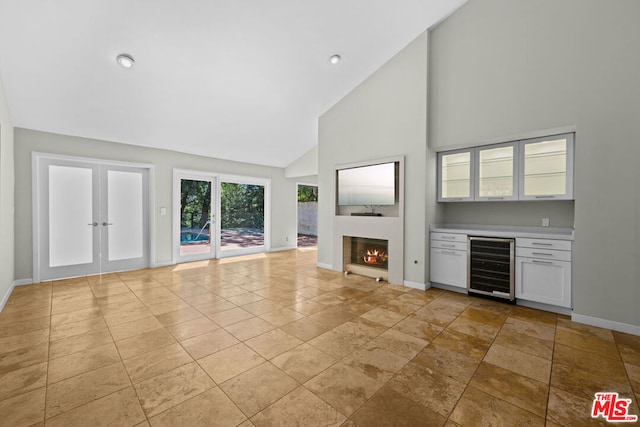 unfurnished living room featuring wine cooler, indoor bar, high vaulted ceiling, and french doors