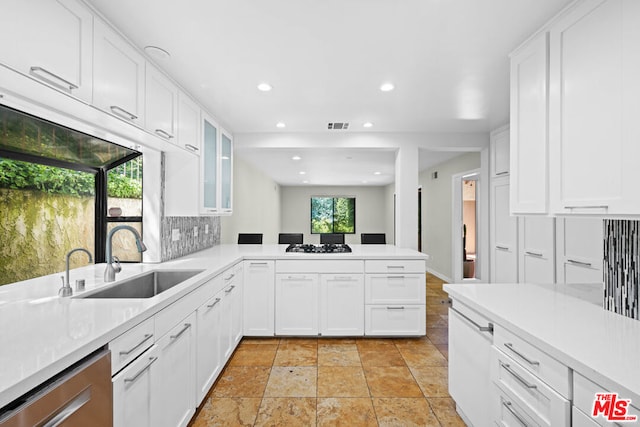 kitchen with sink, white cabinets, decorative backsplash, stainless steel dishwasher, and kitchen peninsula