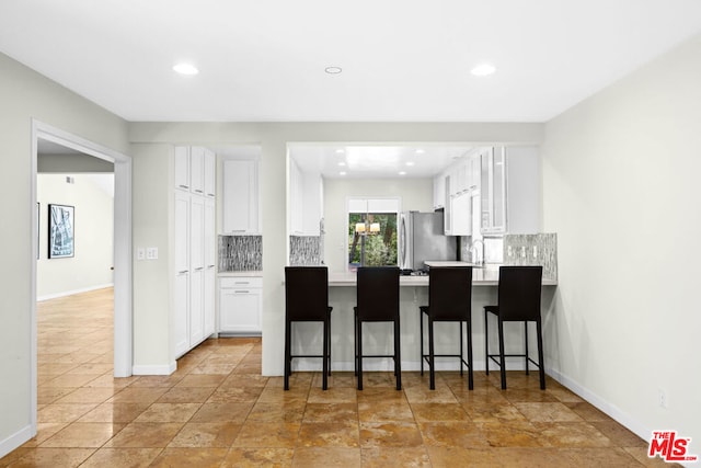 kitchen with a breakfast bar area, stainless steel fridge, tasteful backsplash, white cabinets, and kitchen peninsula