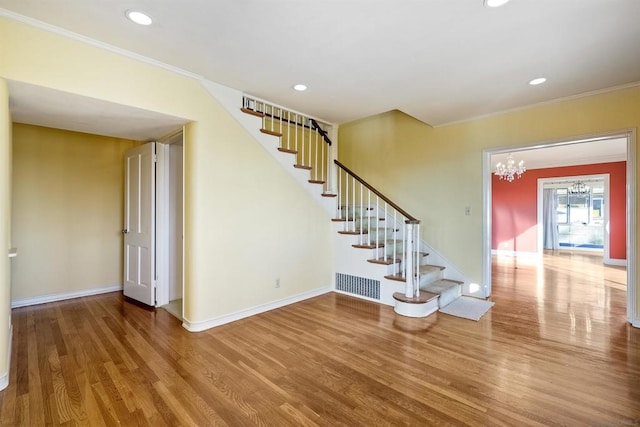 staircase featuring ornamental molding, hardwood / wood-style floors, and a notable chandelier