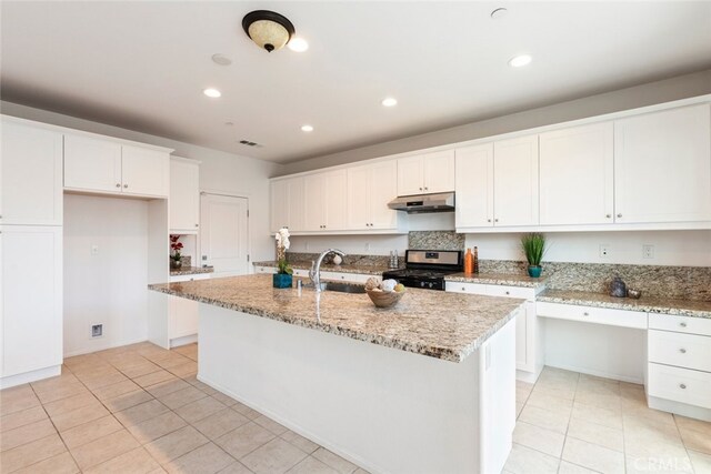 kitchen with stainless steel gas range, sink, a center island with sink, light stone countertops, and white cabinets