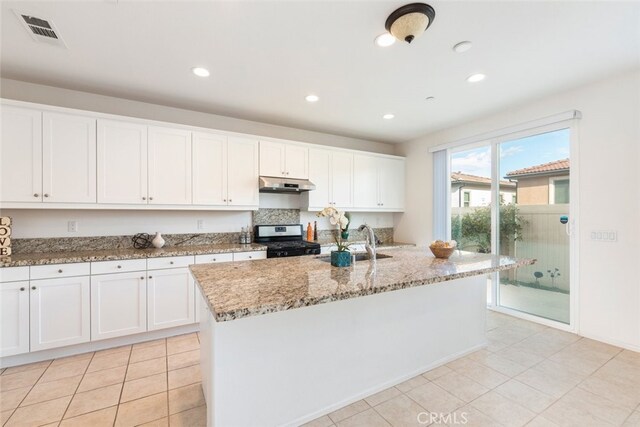 kitchen with sink, light stone counters, white cabinets, a center island with sink, and stainless steel range with gas cooktop