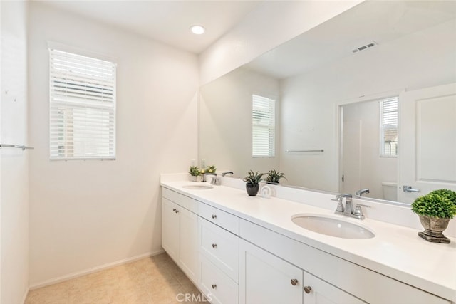 bathroom with double vanity, baseboards, visible vents, and a sink