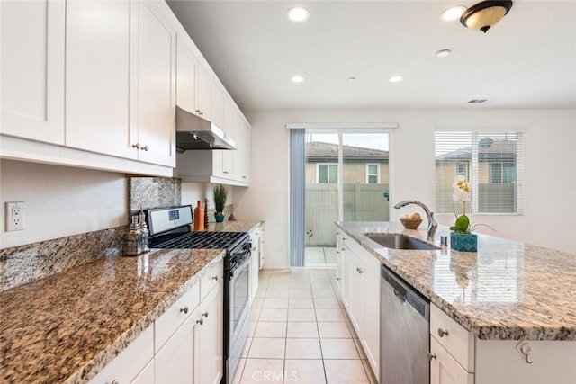 kitchen featuring under cabinet range hood, stainless steel appliances, a sink, white cabinetry, and light stone countertops