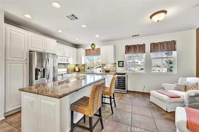 kitchen with stone countertops, light tile patterned floors, a kitchen island, white appliances, and white cabinets