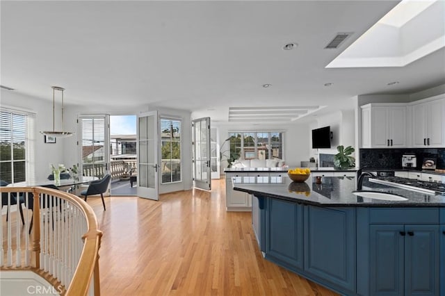 kitchen with blue cabinets, dark stone countertops, pendant lighting, a healthy amount of sunlight, and white cabinets